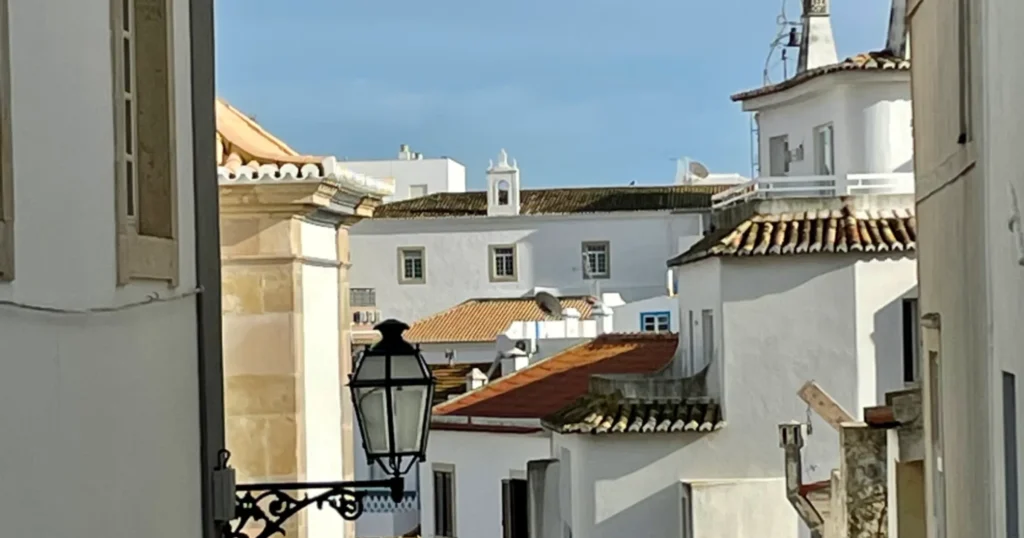 Albufeira street with white buildings with red barrel tile roofs. A lantern in the foreground and buildings in the distance