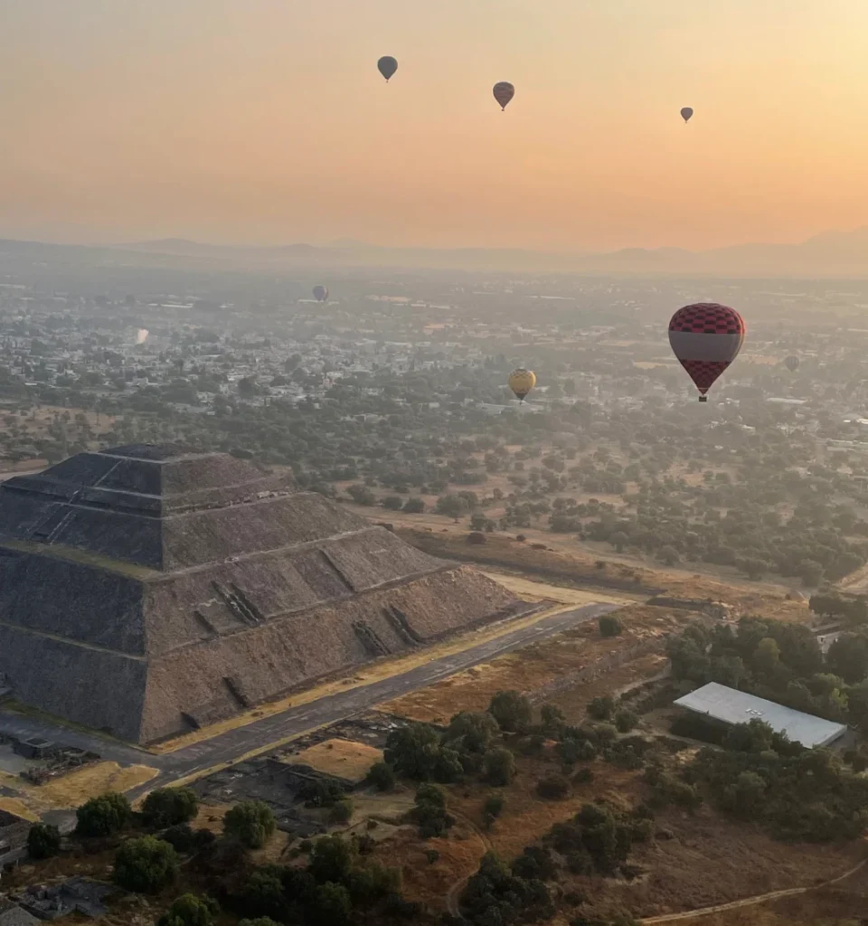 Hot Air Balloon ride over the Teotihuacan ruins in Mexico City. Pyramid off to the left with hot air balloons flying above in the sunrise
