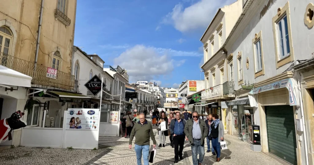 Street in Albufeira Portugal with people walking towards the camera. Shops and restaurants line the streets in white buildings