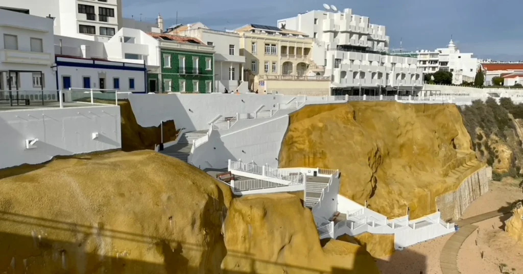 Albufeira Portugal, white walled stairs going down the beach cliff with white and green and pink buildings on the top of the cliff