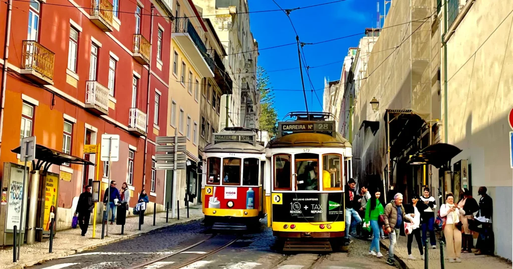 Lisbon Cable Car image of two cable cars passing each other in the street. A red one on the left and a black one on the right.