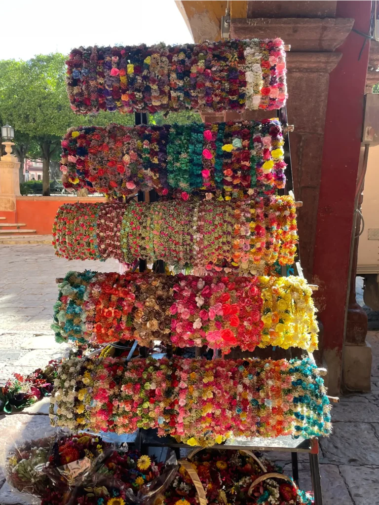 Racks of colorful handmade flower crowns for sale on the sidewalk in the Jardin de Allende, San Miguel de Allende