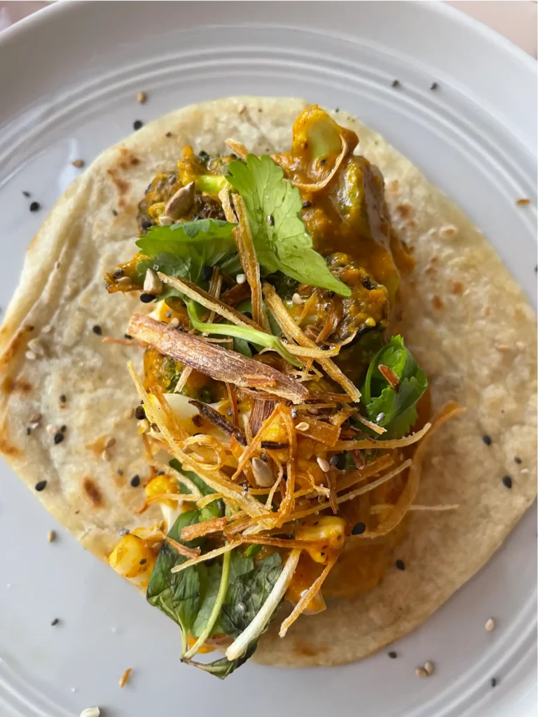 Taco image on a white plate, naan bread tortilla with chicken and orange and green colored toppings