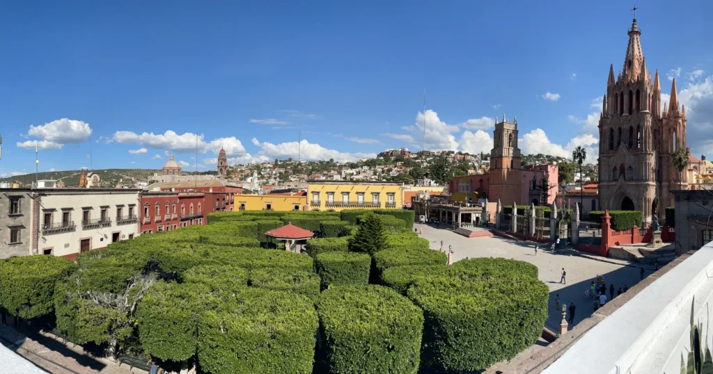 Jardin de Allende over head view with buildings around the park, manicured trees below and the Parroquia de San Miguel Arcángel to the right