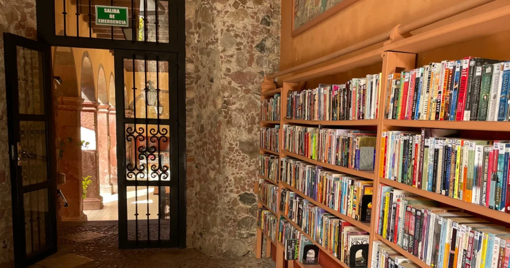 San Miguel de Allende Public Library image of bookshelf with stone wall, wrought iron gate and courtyard in the background