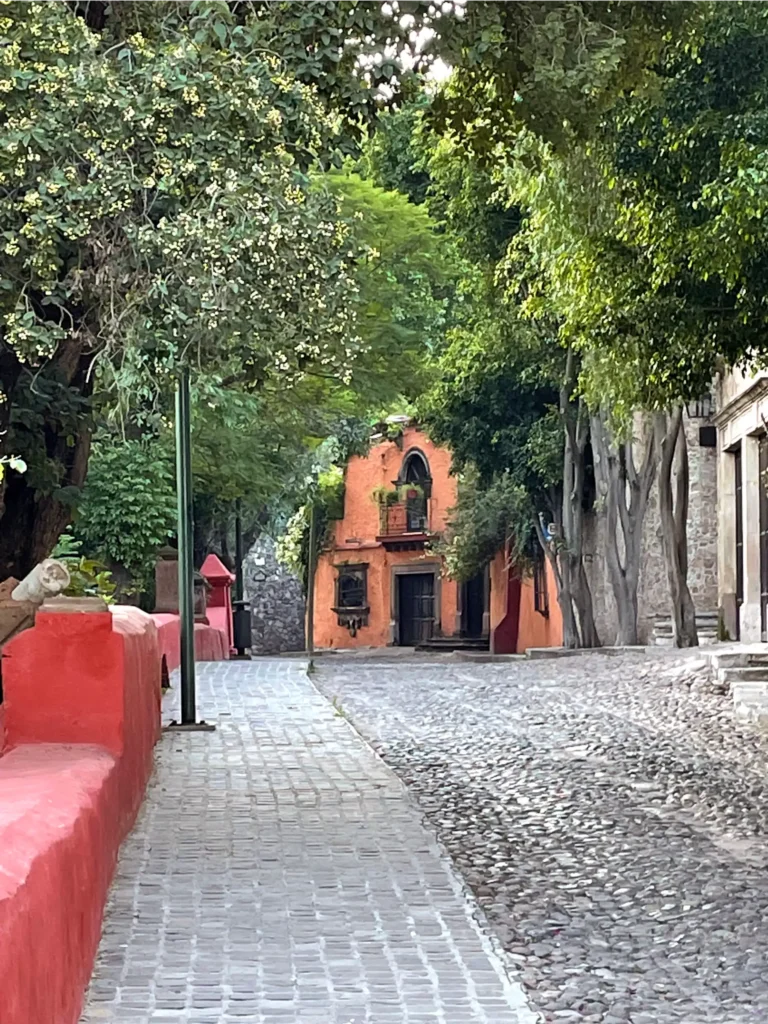 Benito Juarez Park view of cobblestone street with red wall along the left and a bright stone colored house in the distance