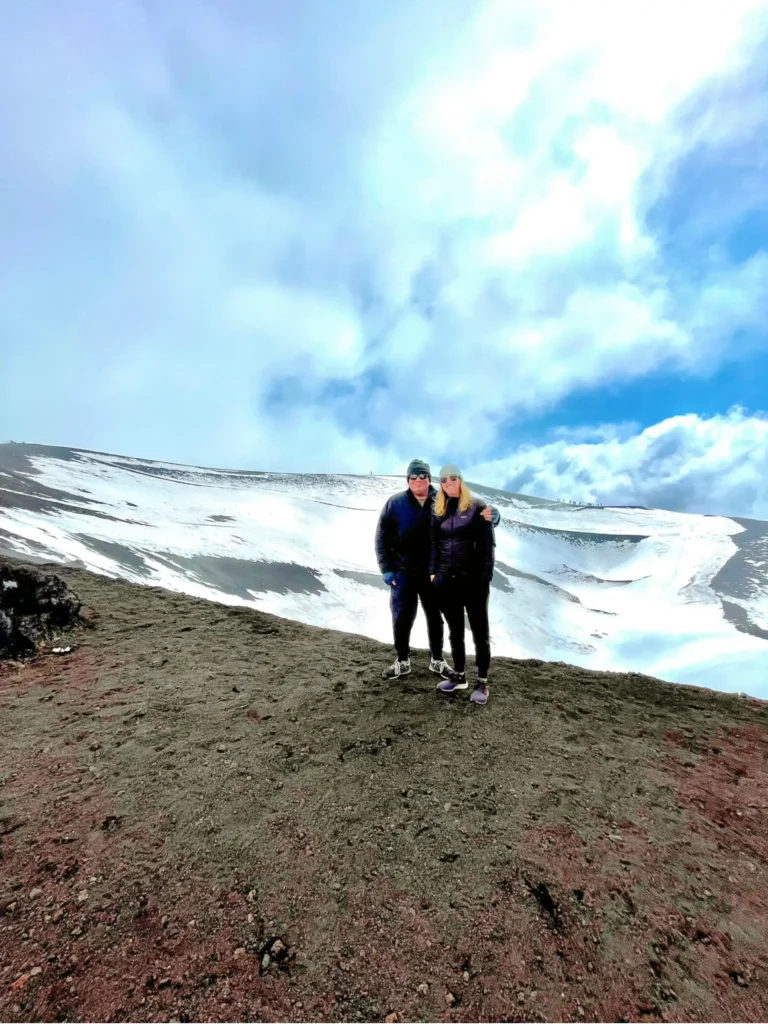 Two Traveling After One standing on the edge of the crater atop Mt Etna volcano in Sicily. Snow in the background