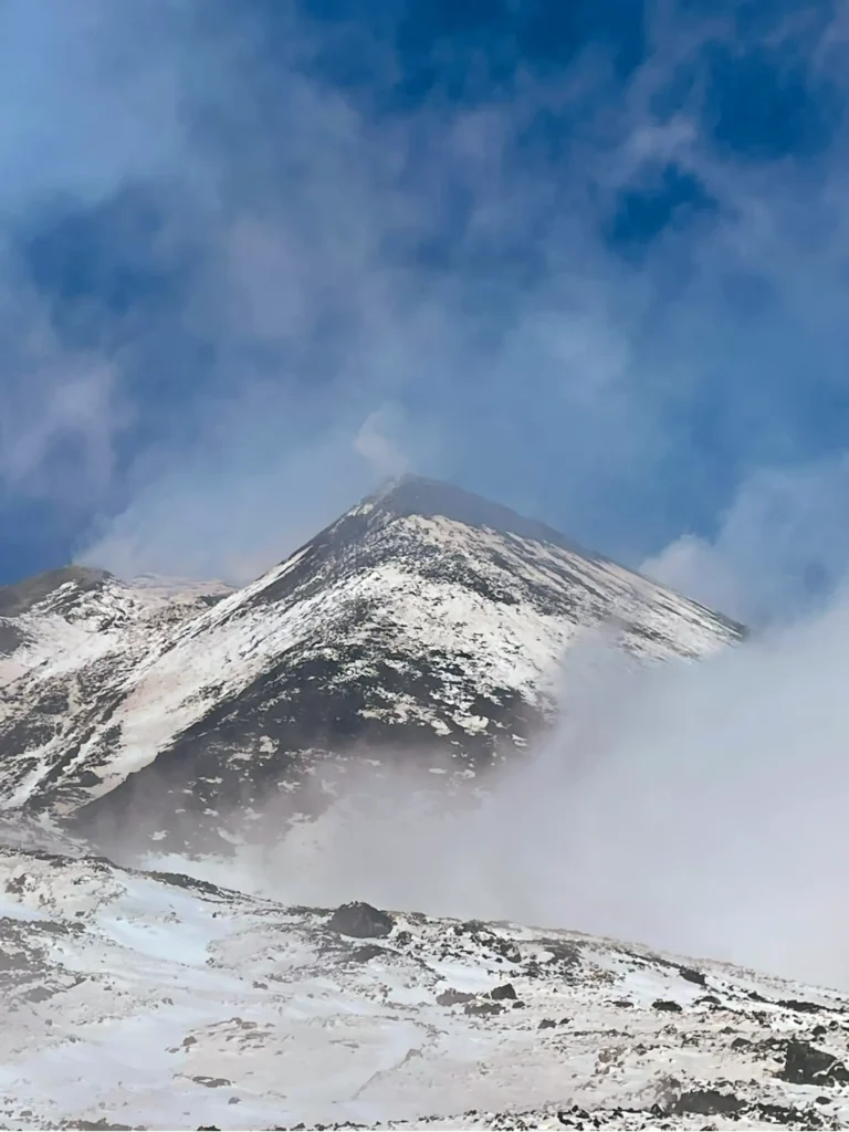 Image of the new peak of Mount Etna volcano in Sicily with wispy clouds surrounding and some smoke coming from the top