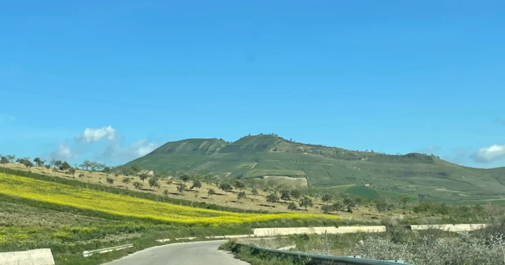 empty two lane road in Sicily with a curve to the right and a mountain in the background
