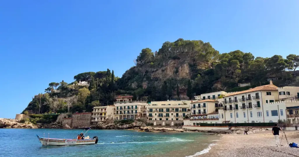 Taormina Beaches, Mazzano Beach hotels in the background lining the edge of the beach with dark sand and crystal blue water
