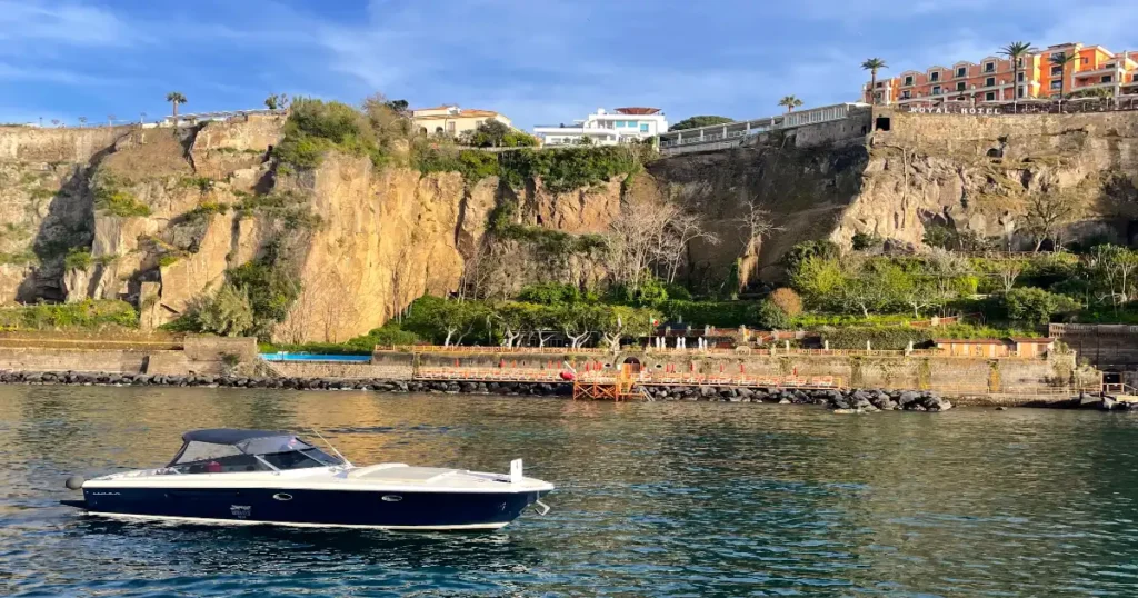 blue boat in water in front of Sorrento cliffs