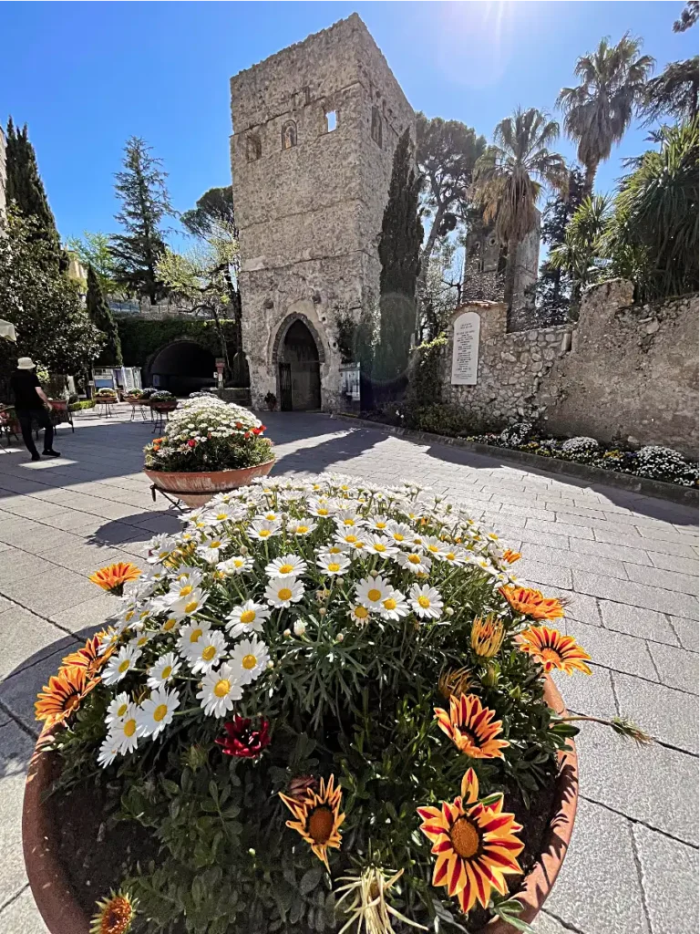 Planter with colorful flowers in the foreground with stone building in the background in Ravello