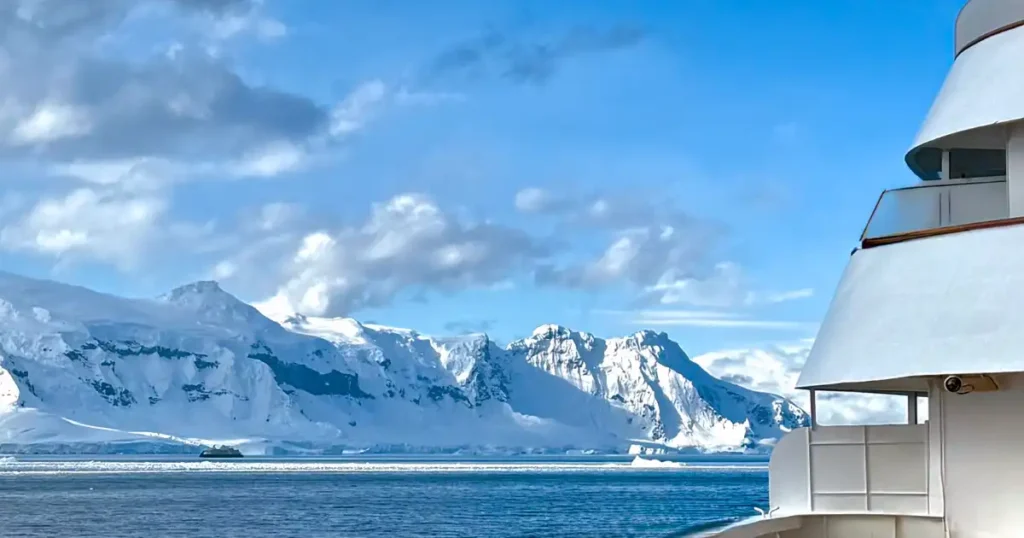 Cruising through Antarctica with mountain range and small ship in ice field in foreground